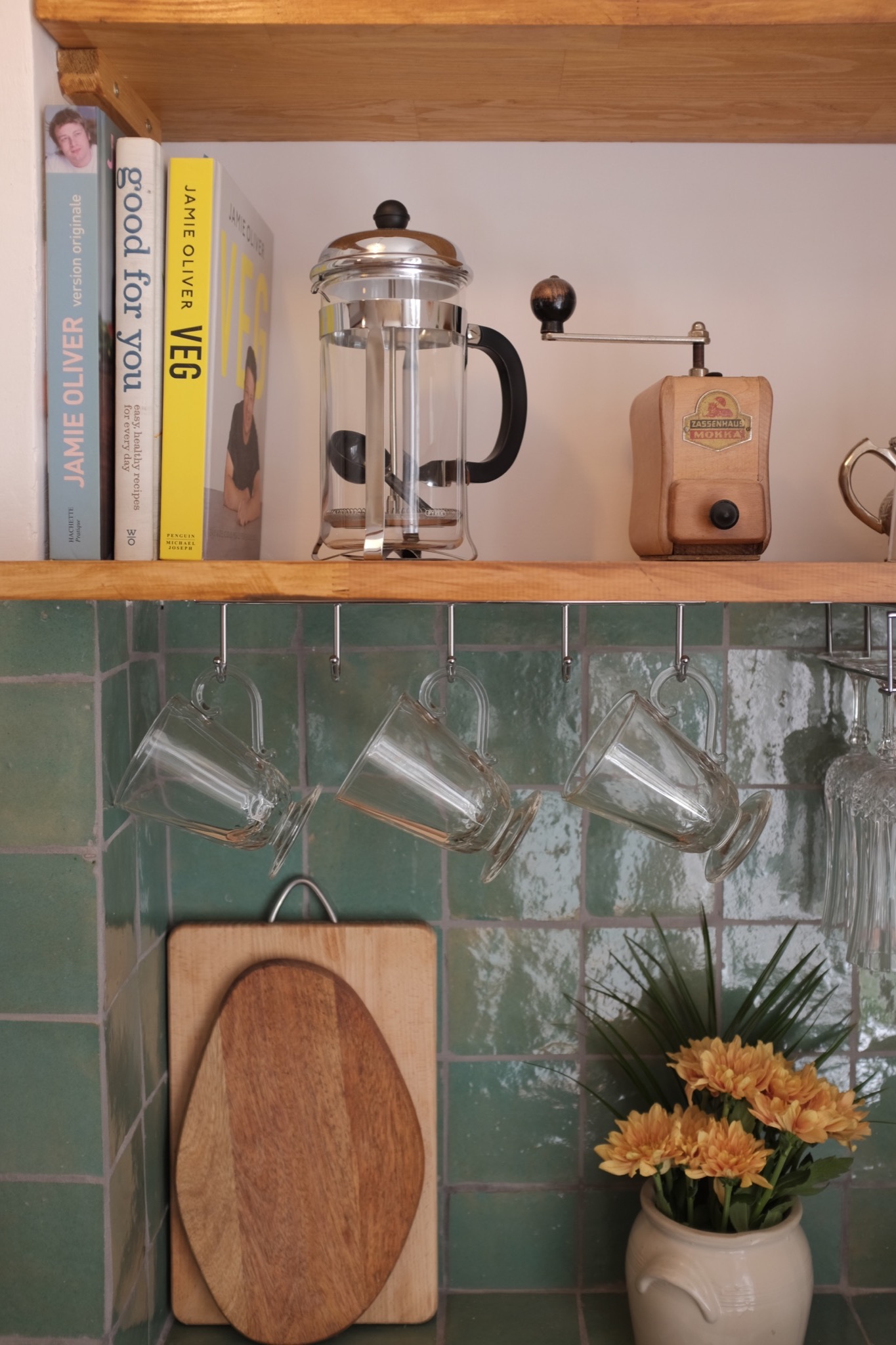 French press and hand grinder on an oak shelf above green zellige tile