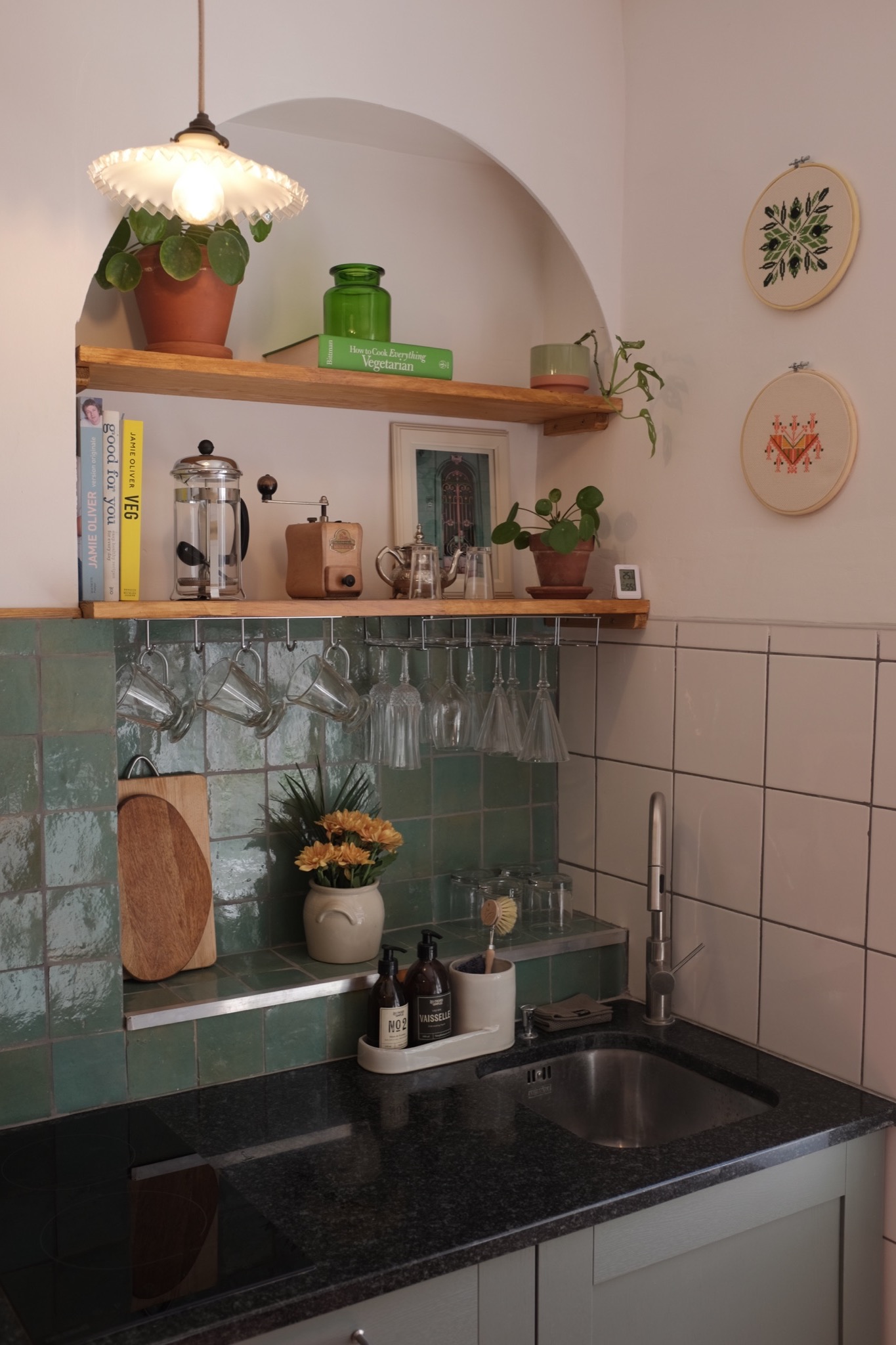 Kitchen with green zellige tile, black granite counter and hanging glassware