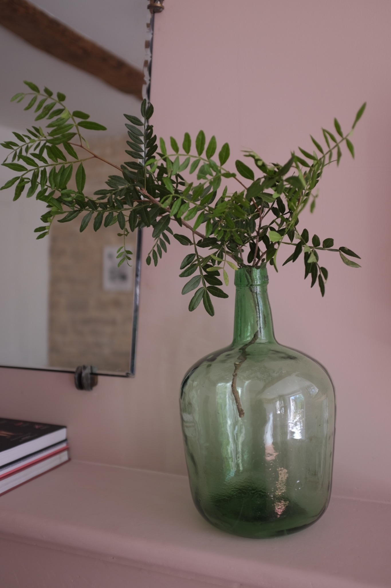 Green glass demijohn holding garden cuttings on a pink mantel