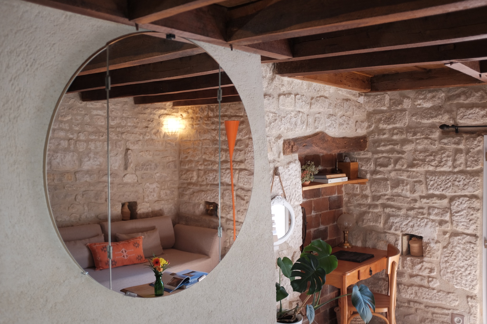 Round mirror reflecting the sitting corner and exposed beams