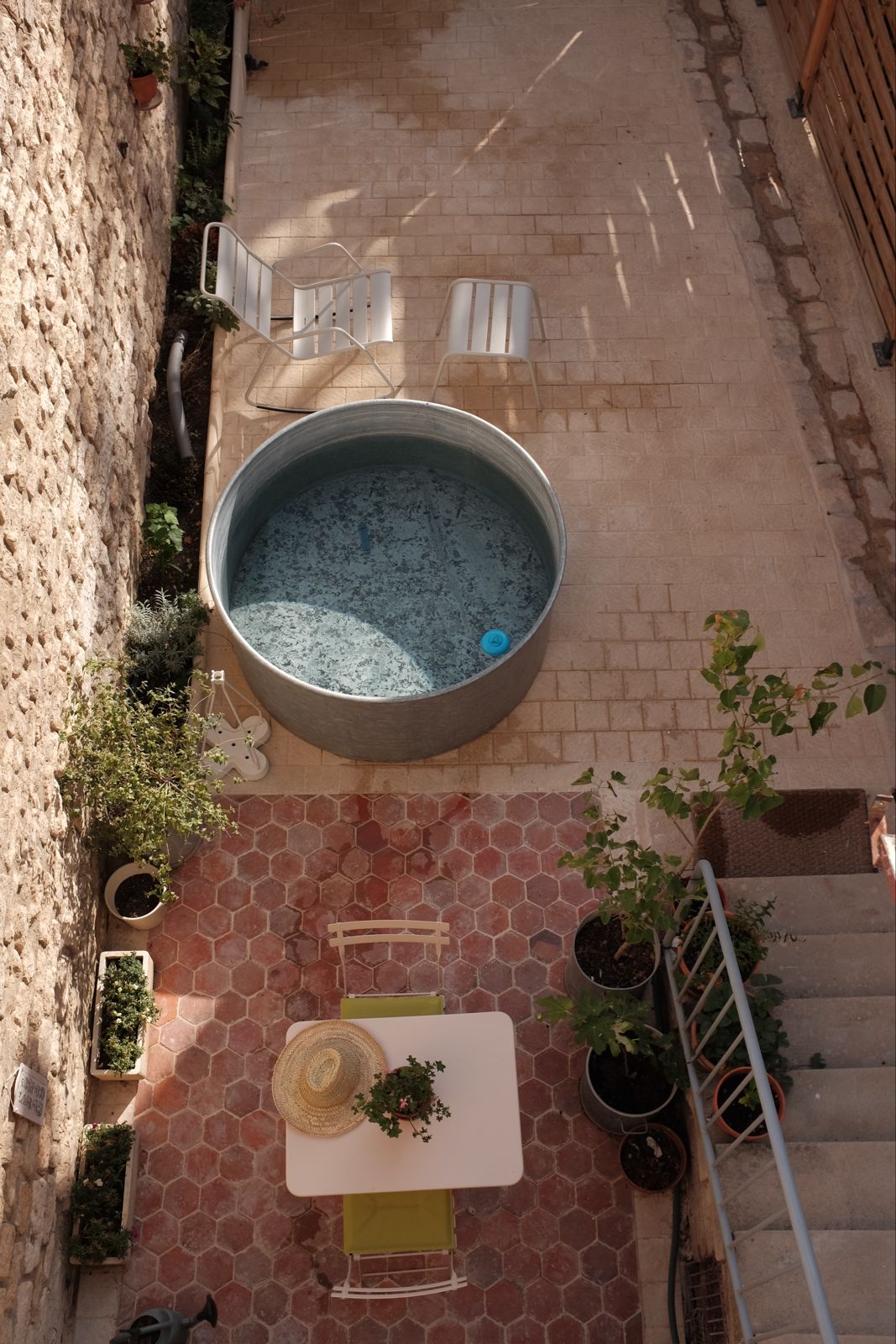 Walled patio with cowboy pool, bistro table and potted plants seen from above
