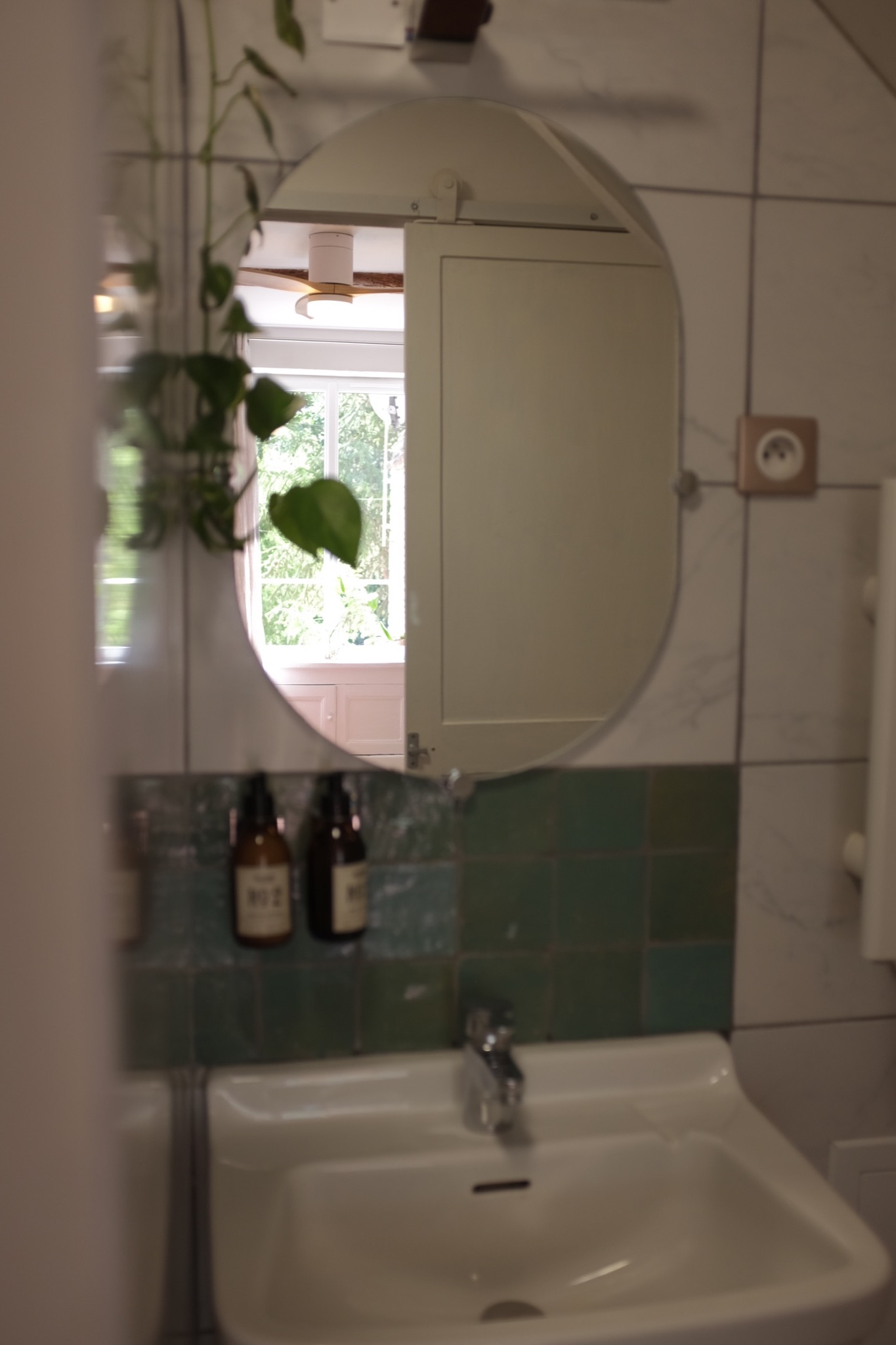 Bathroom basin and oval mirror with green zellige tile and open window