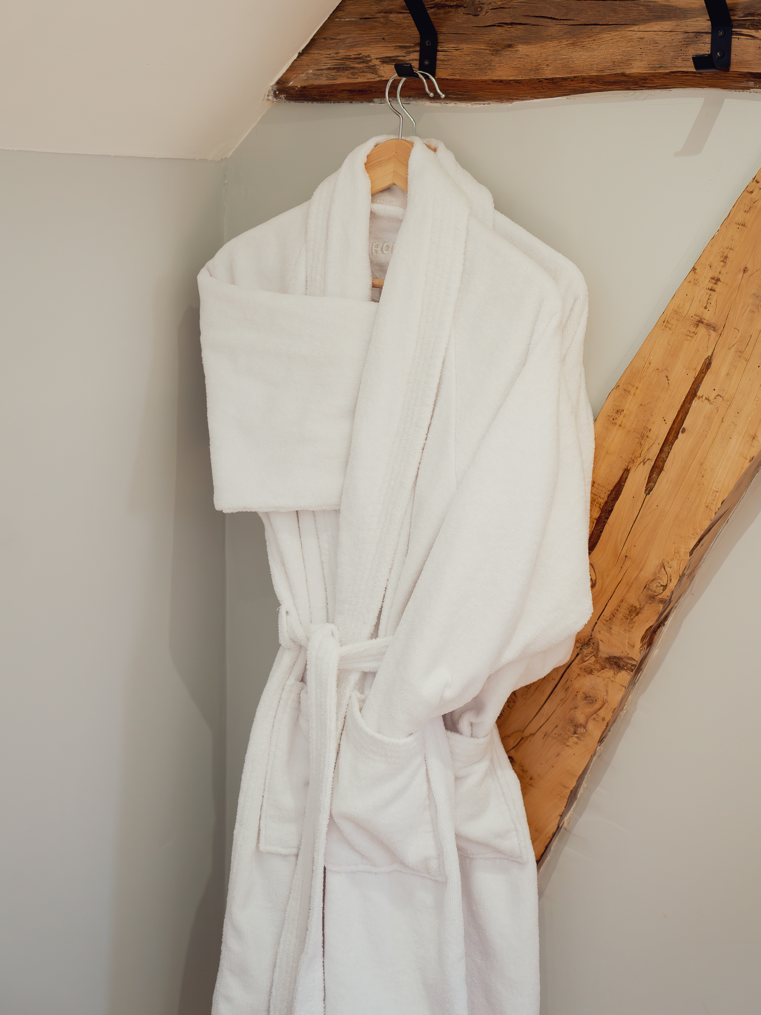 Plush white bathrobes on wooden beam