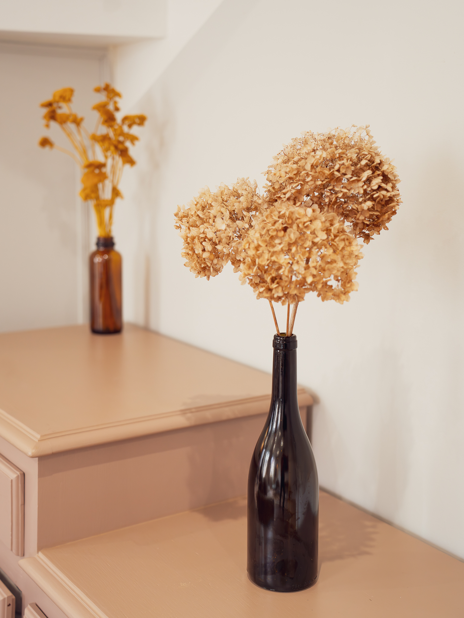 Dried hydrangeas in amber bottles on mauve dresser